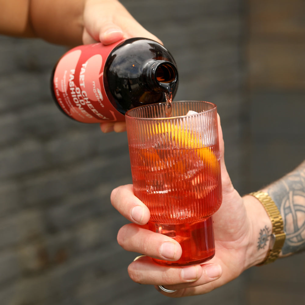 hand pouring modica tart cherry old fashioned mix in a cocktail