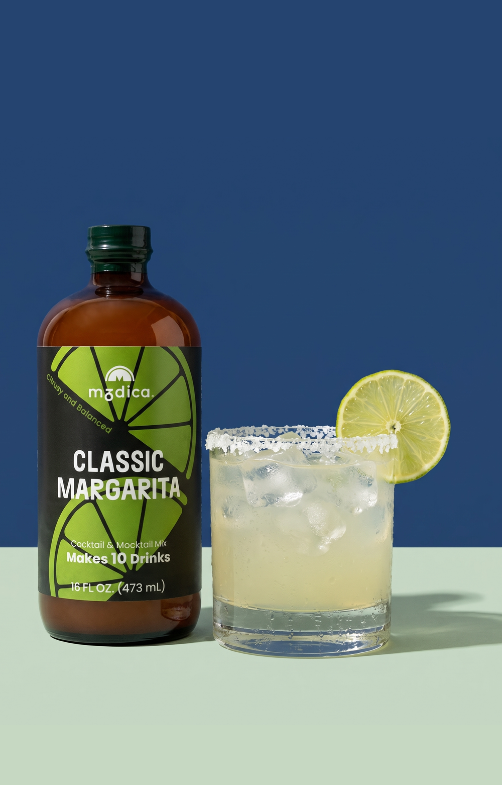 Modica Classic Margarita mixer bottle next to a margarita on the rocks with a salt rim and lime wheel